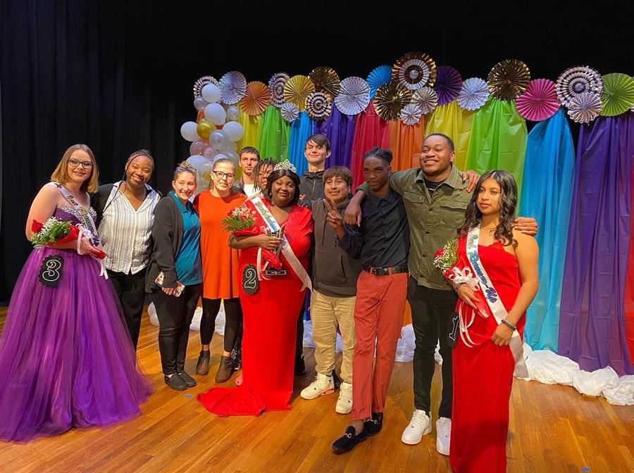   A group of students pose and smile to the camera while on stage after the program.